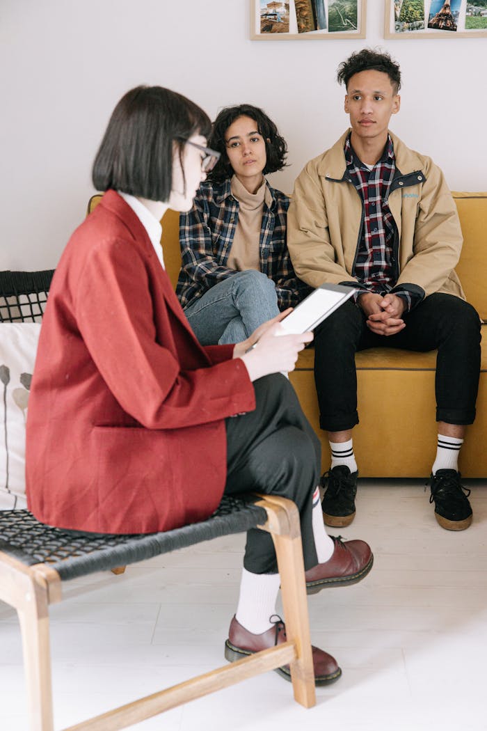 A therapist leads a counseling session with a young couple seated on a couch.