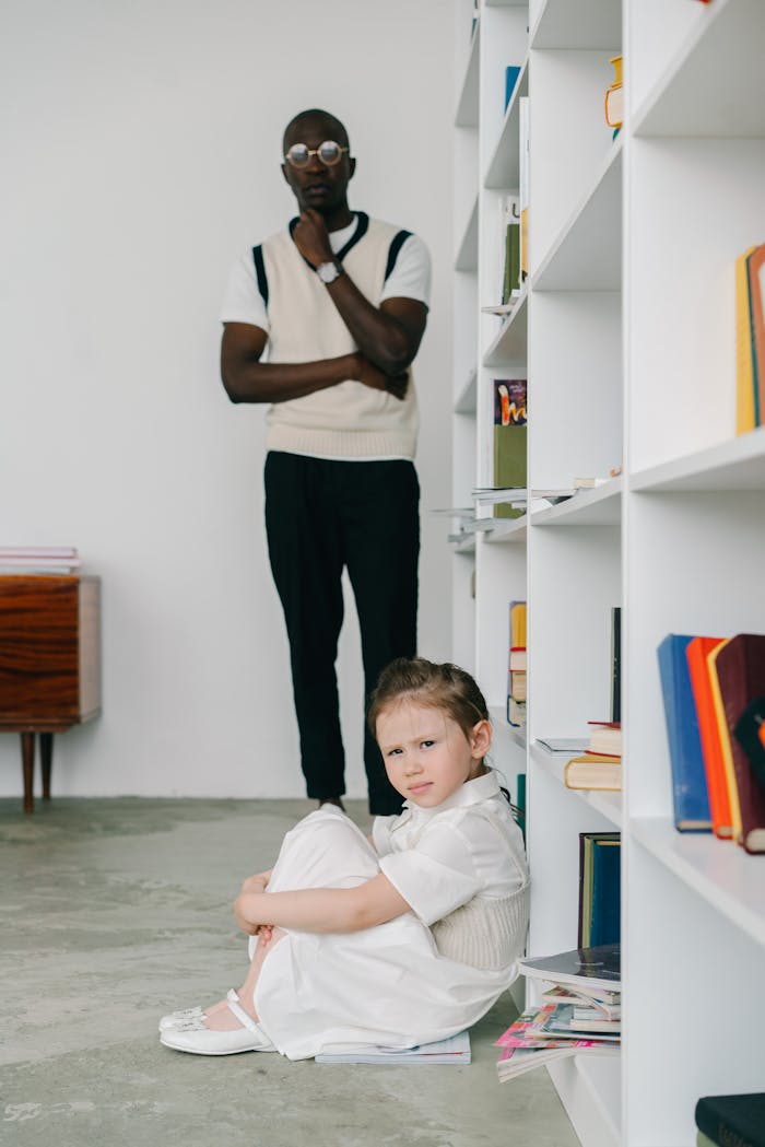 A child sits thoughtfully while a therapist observes in a counseling session.