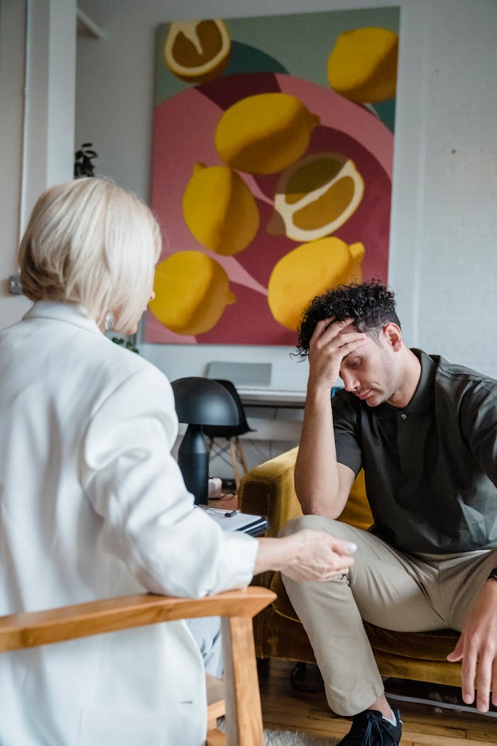 A young man in therapy expressing stress and concern during a session with a psychologist in an indoor setting.